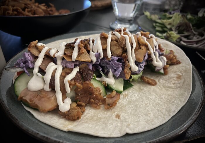 Kycklingkebab i tortilla med rödkål, gurka, kebabsås och sallad på en tallrik.