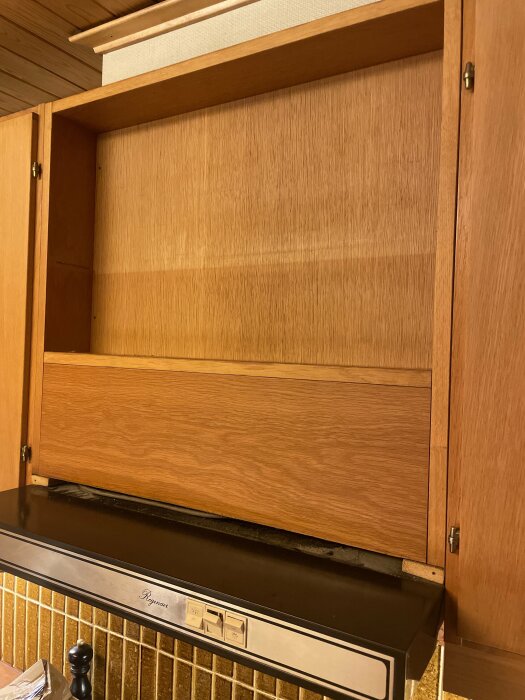 Träskåp ovanför en Husqvarna köksfläkt, delvis öppnad, visar en inbyggd fläktkåpa i ett gammalt kök från Canadaköket.