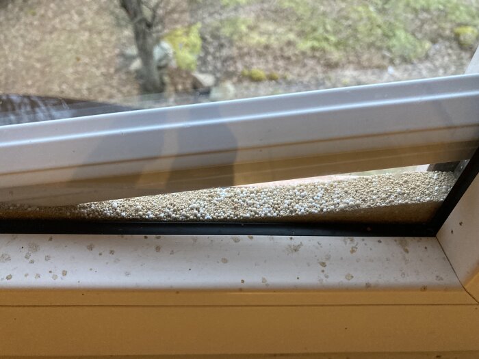 Fönsterkarm med isolering som ser ut som små kulor, sedd från insidan av ett gammalt hus.