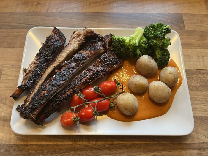 Revbensspjäll med kanarisk potatis, rookiesås, körsbärstomater och broccoli på en tallrik.