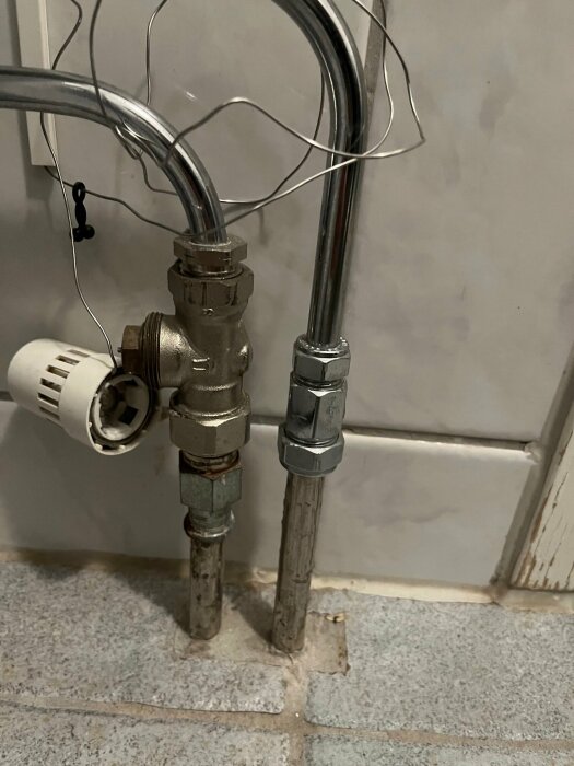 Golvvärmeanslutning med termostatventil och rör, som är en del av vattenburen golvvärme i ett badrum.