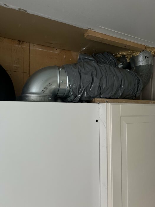 Ventilationssystem med silverfärgat rör lindat i plast i ett hem, nyinstallerat aggregat, träplank som stöd ovanpå.