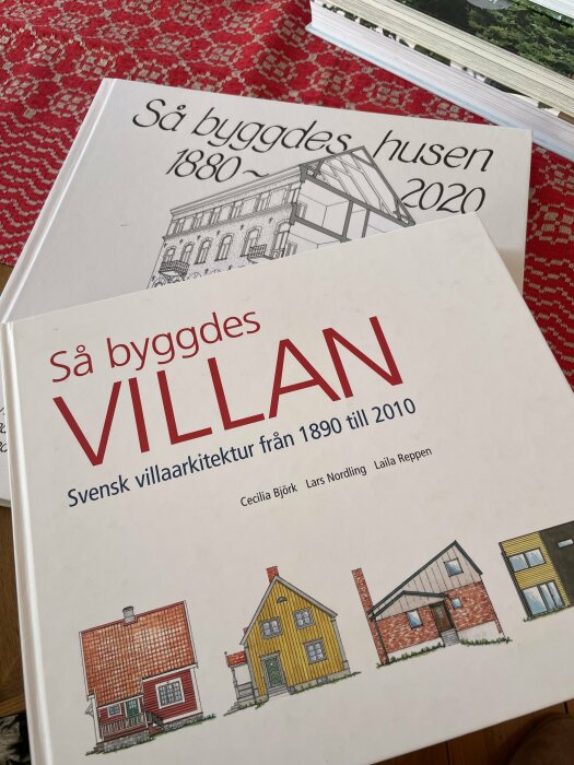 Närbild på två böcker om svensk arkitektur: "Så byggdes VILLAN" och "Så byggdes husen 1880-2020" på ett rött mönstrat underlag.