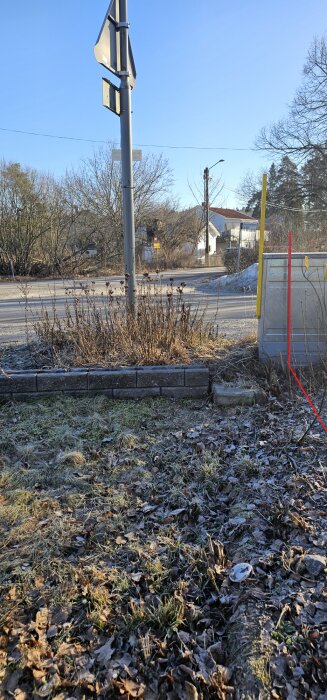 Elskåp blockerar infarten till en tomt, omgiven av torrt gräs och vissna växter, delvis skuggat av angränsande träd och stolpar.