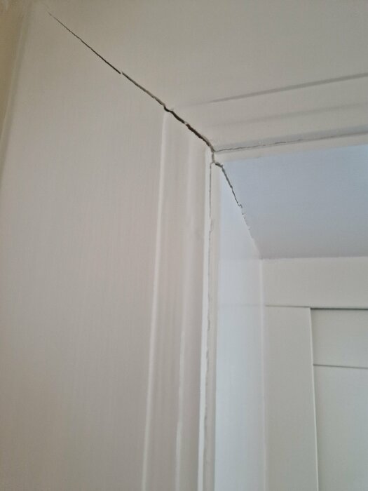 Sprickor i hörnet av en vit fönsterkarm i ett äldre hus, troligtvis orsakade av temperatur- och luftfuktighetsförändringar.