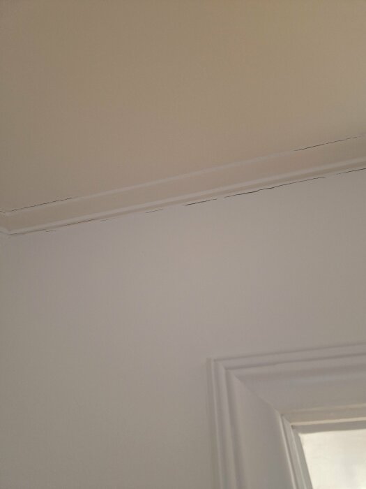 Sprickor i vävda taket nära taklisten i ett trähus från 1920, synliga ovanför fönsterram i ett rum med torrare luft.