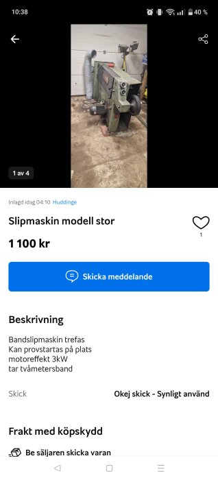 Stor bandslipmaskin trefas med motor, stående på verkstadsgolvet.