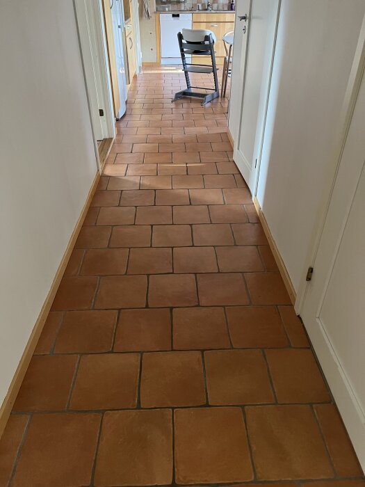 Gul/orange kakelgolv i korridor och kök, med dörröppningar och möbler synliga i bakgrunden.