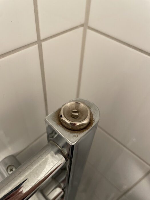 Metallkomponent på toppen av en rörledning installerad mot kakelvägg, potentiell vattenpåfyllningspunktsindikator.