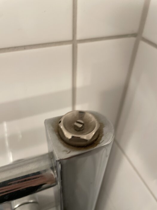 Närbild på en del av en metallisk badrumsarmatur vid kaklade väggar. Ett lock verkar saknas på den högra ventilen.