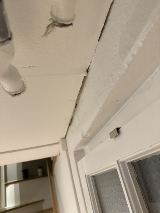 Springor mellan tak och vägg i källare, med synliga rör och steg i bakgrunden.