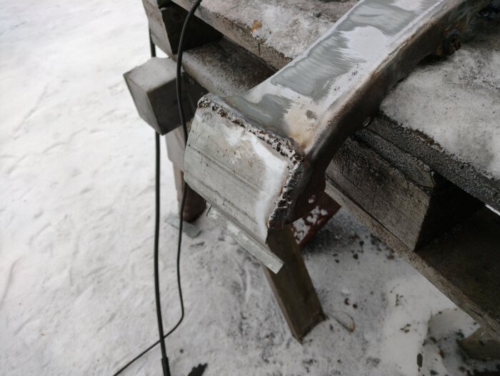 Reparerad framskärm med svetsad ersättningsdel monterad på ett bord bland snö.