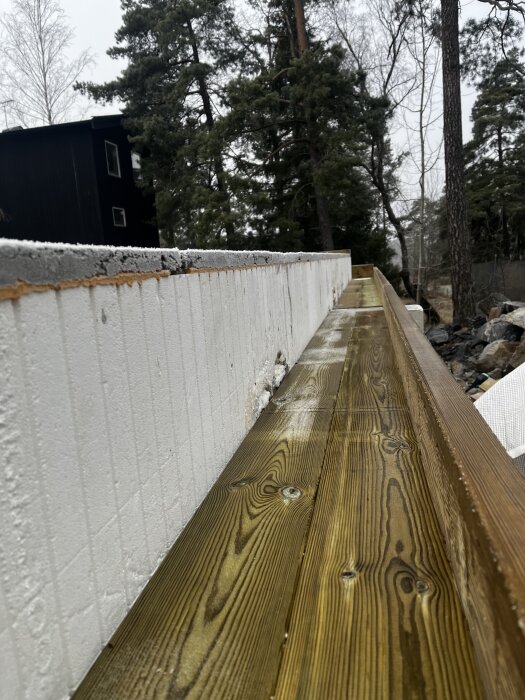 Träplankor med en underliggande konstruktion av vit isolering, del av pågående byggprojekt utomhus. Skog i bakgrunden.