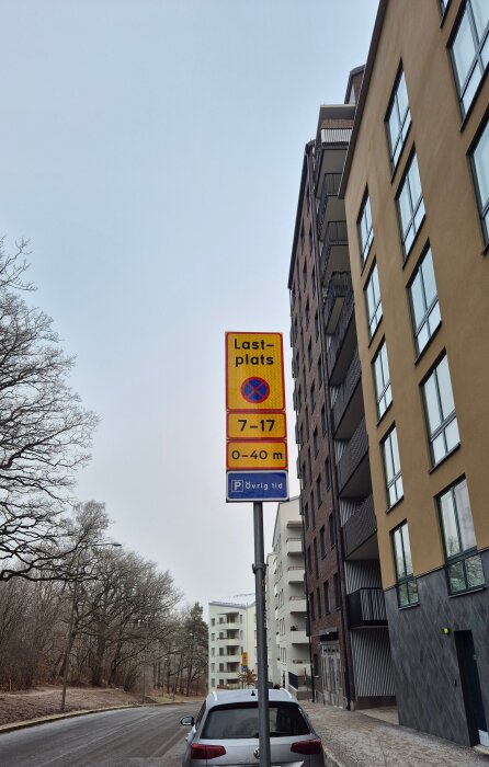 Vägskylt vid gata bredvid byggnad visar lastplats och tid 7-17, övrig tid tillåten parkering. En bil syns parkerad vid trottoaren.