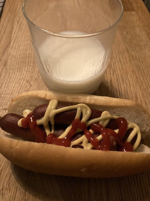 Kokt korv med senap och ketchup i bröd, serverad med ett glas mjölk på ett träbord.