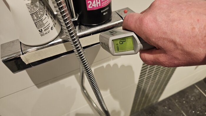 Hand som använder en digital termometer för att mäta temperaturen på en duschblandare.