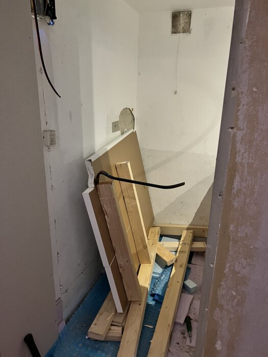 En hörna av ett halvrivet badrum med borttagna trädelar och verktyg på golvet inför renovering.