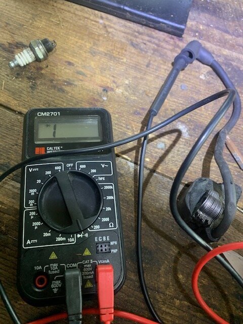 Multimeter visar "1" på träbord, med tändkabel och tändstift bredvid.