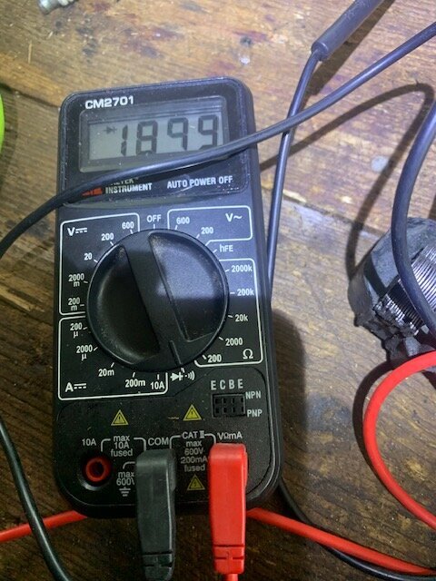 Multimeter visar ett värde på 1899 ohm, placerad på ett träbord, med anslutna svarta och röda testkablar.