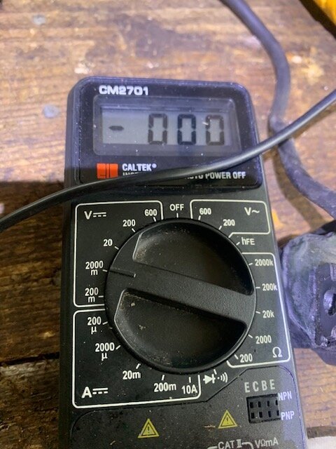 Multimeter visar noll på display, placerad på ett bord med synliga sladdar.