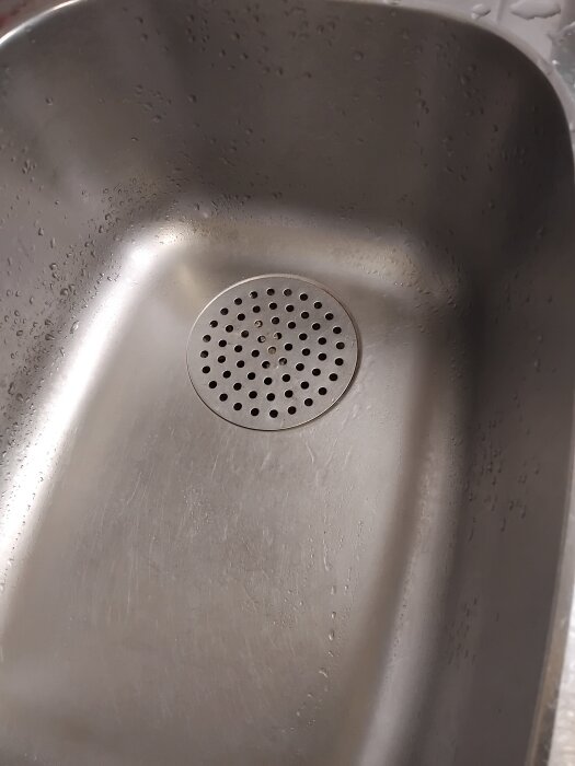 Köksvask med avloppssilen i mitten, omgiven av vattenstänk. Silen orsakar lågt flöde och det är svårt att rengöra under den.