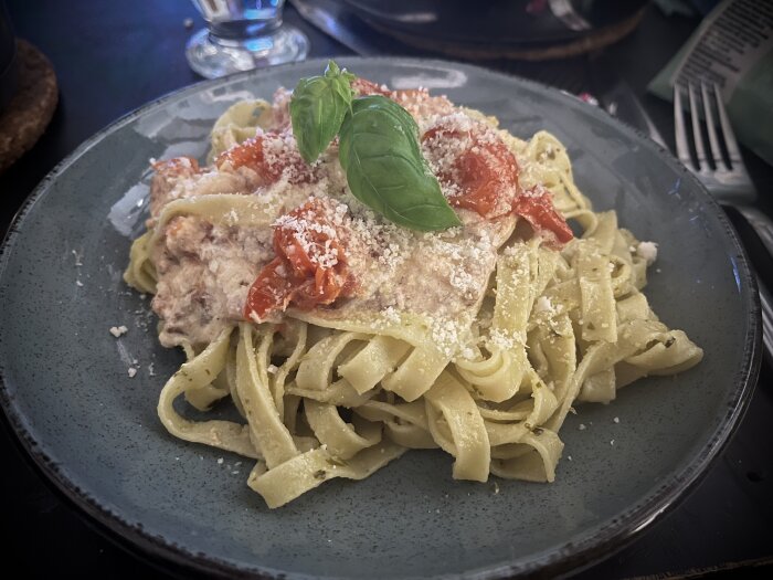 Pasta med burrata, bacon och ugnsrostade tomater toppad med riven parmesan, serverad på en tallrik.