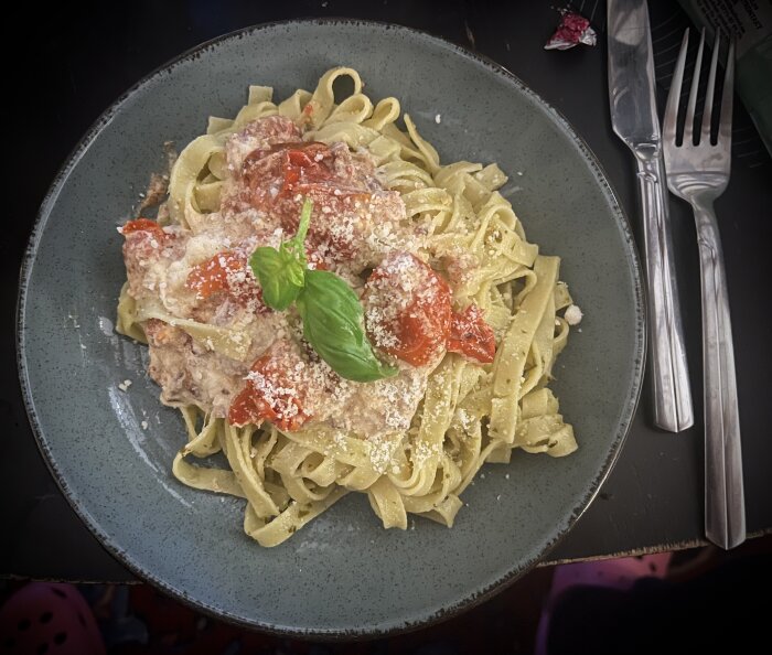 Pasta med burrata, bacon och ugnsrostade tomater, toppad med riven parmesan och basilika på en tallrik.
