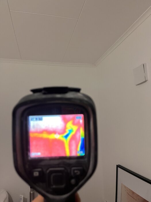 Termografikamera visar temperaturskillnader i takhörn med färger; röd och blå indikerar möjliga tecken på isoleringsproblem.