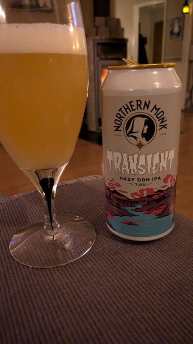 Ett glas med öl bredvid en burk Northern Monk Transient Hazy DDH IPA, 7.0%, står på ett bord.