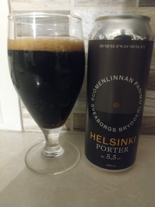 Ett glas fyllt med mörk öl och en burk märkt "Helsinki Porter" från Sveaborgs Bryggeri står på ett bord.