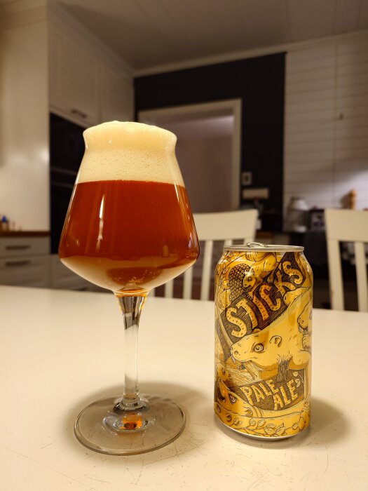 Ett glas öl med skum bredvid en burk märkt "Stick's Pale Ale" på ett köksbord.