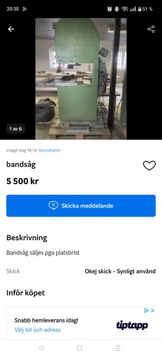 Grön bandsåg placerad på en pall i en verkstadsmiljö med verktyg och bord i bakgrunden.