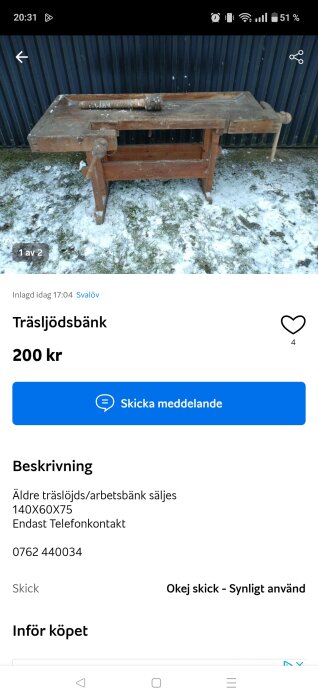 Gammal slöjdbänk av trä på snötäckt mark framför en mörk vägg.