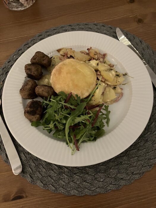 Tartiflette med köttbullar och grönsallad på en vit tallrik.