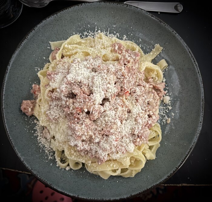 Krämig salsiccia-pasta med grädde och vitt vin, toppad med rikligt riven ost på en grå tallrik.