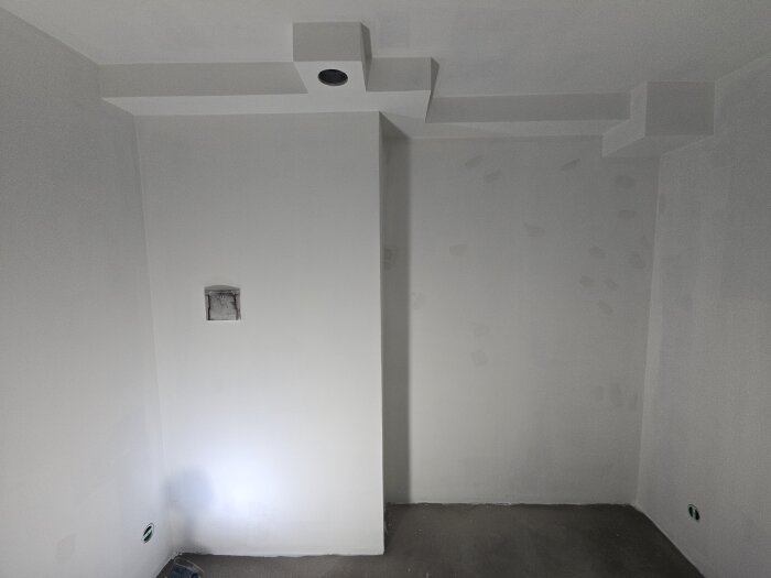 Nymålat förråd med grundmålade väggar och tak, synlig lampinstallation samt ett ventilationsrör i arbetets början.