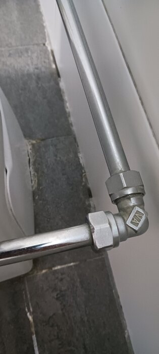 Ett L-format kopparrör som möts vid en vägg med mörkt klinkergolv.