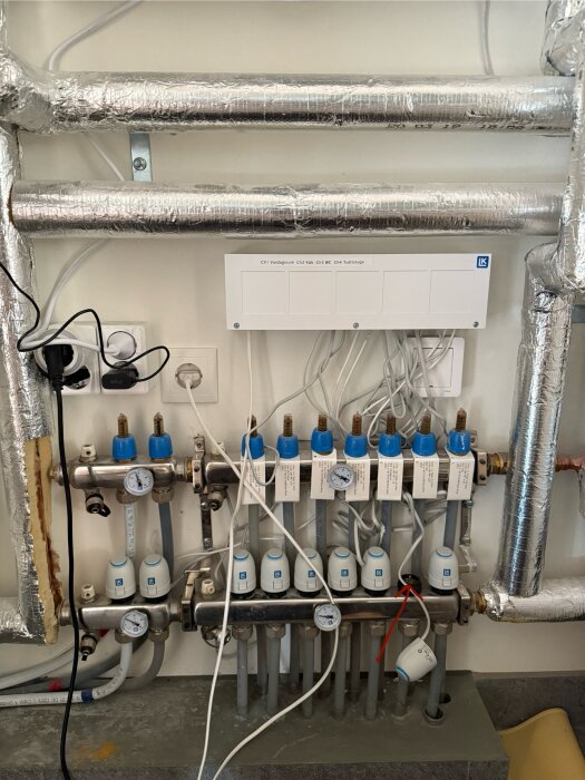Värmeinstallation med termostater, rör och ställdon i golvvärmesystem. En röd pil markerar ett område för eventuell felsökning.