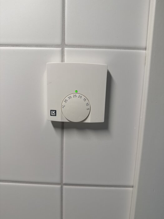 Termostat på väggen med grön lampa som lyser, inställd på cirka 18 grader.