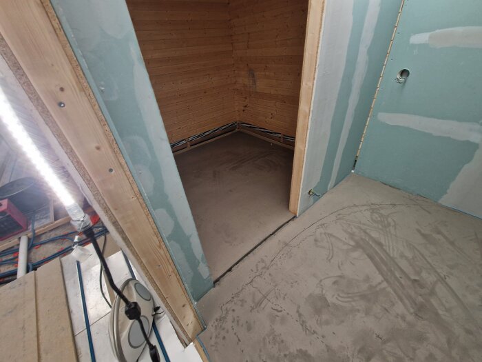 Under construction room with newly concrete-smoothed floor showing grooves. Walls are partially finished with drywall. Exposed wiring visible.