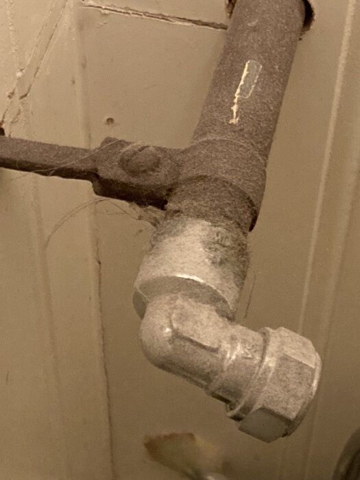 Dammigt mörkt rör med skrapad yta och silverfärgat fäste i ett gammalt badrum, potentiellt ett avklippt och plugget vattenrör från före 2008.