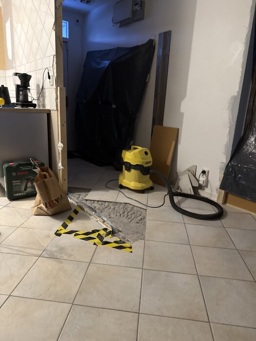 Renovering av kök med delvis avlägsnat klinkergolv, synligt ljust material undertill. Verktyg och byggmaterial i bakgrunden.