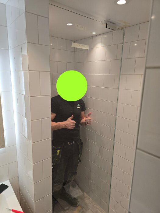 Installatören ger tummen upp i en nyinstallerad duschkabin med vita plattor och en glasvägg.