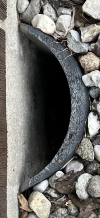 Halvrör av metall i en krypgrund omgivet av stenar, för ventilation.