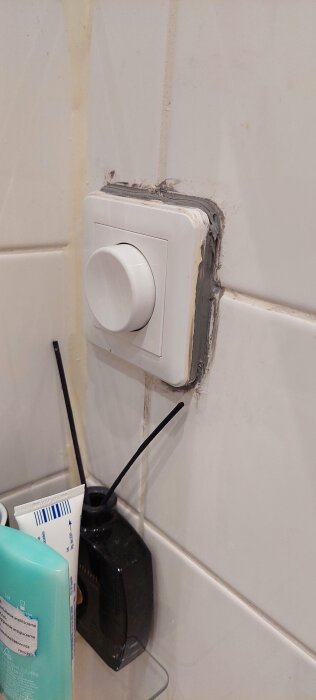 Ljusströmbrytare på vägg med synligt gammalt fog; badrumstillbehör i förgrunden.