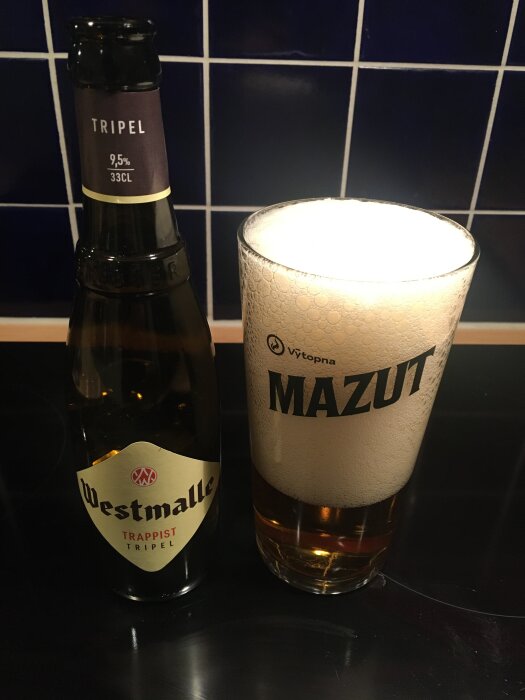 Flaska Westmalle Trappist Tripel 9,5% och ett glas öl på en mörk yta.