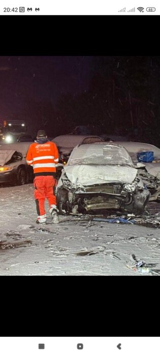 Bilolycka på snötäckt väg, fronten av en bil är kraftigt demolerad. En person i orange reflexjacka står framför bilen.