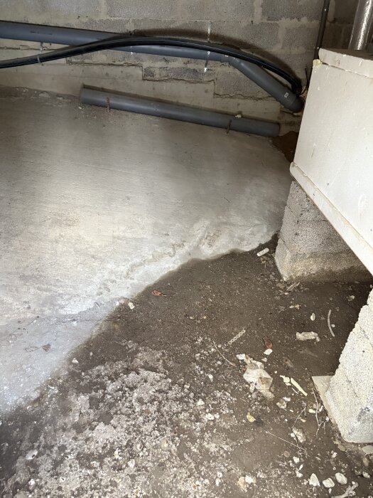 Utrymme i byggnad med betonggolv, synliga rör och en vägg av betongblock; ingen tydlig skada eller påväxt observeras.