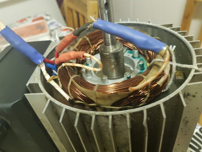 Närbild på elmotor med tre lindningar kopplade med färgade kablar, blå och röda isoleringar synliga. Lindningar på rödsvartbeige bakgrund.