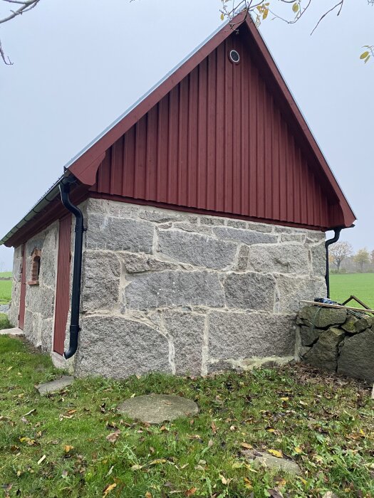 Rött hus med putsad stenmur med KC-bruk från Byggmax, omgivningen gräsbevuxen. Gården i bakgrunden renoverad på 70-talet.